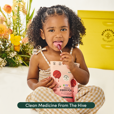 Child holding a package of 'Beekeeper Naturals' fiber pops with flowers and a yellow container in the background.