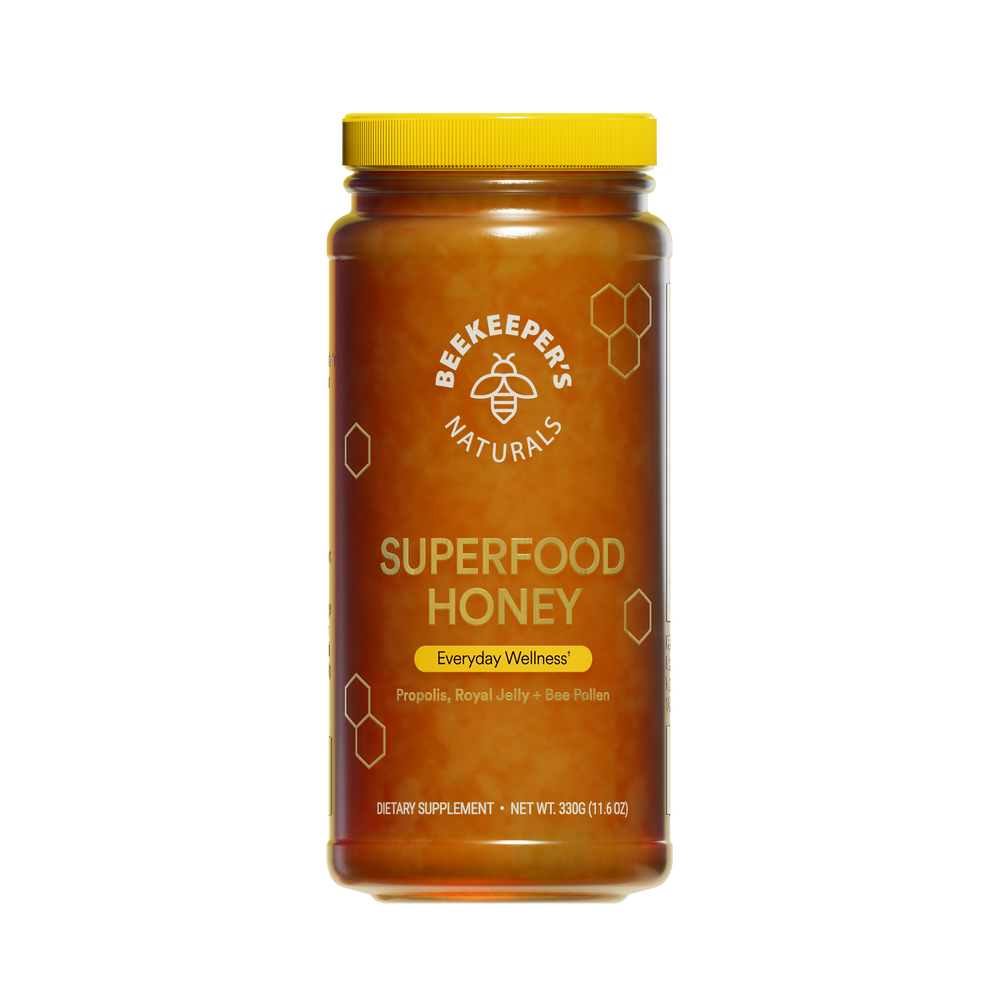 A jar of Beekeeper's Naturals Superfood Honey with a yellow lid, honeycomb patterns, and labels indicating propolis, bee pollen, and royal jelly as ingredients.