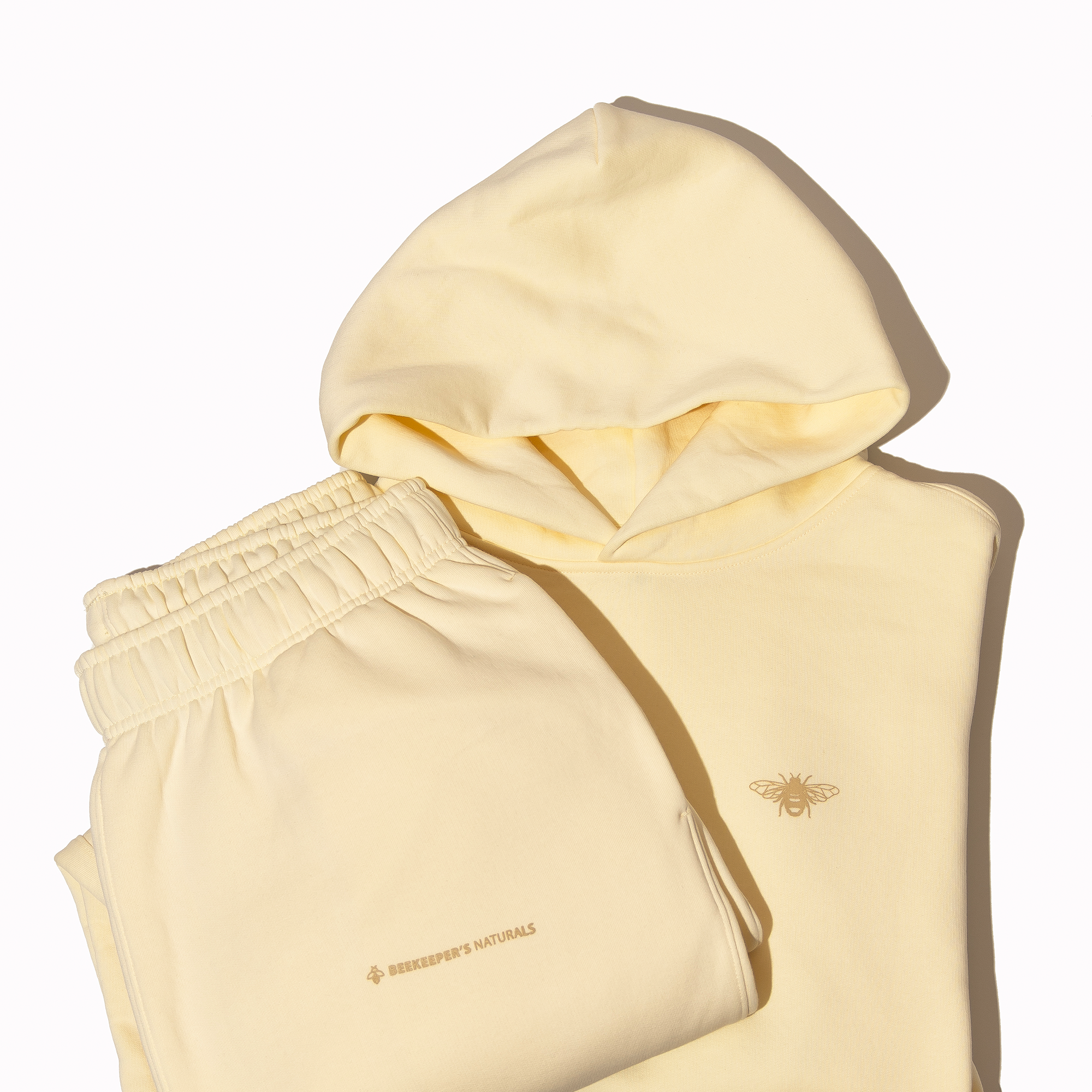 Cream hoodie and pants set with a bee logo on a white background