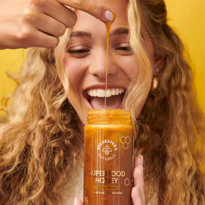 Enthusiastic woman enjoying Beekeeper's Naturals Superfood Honey, highlighting its deliciousness & natural wellness benefits