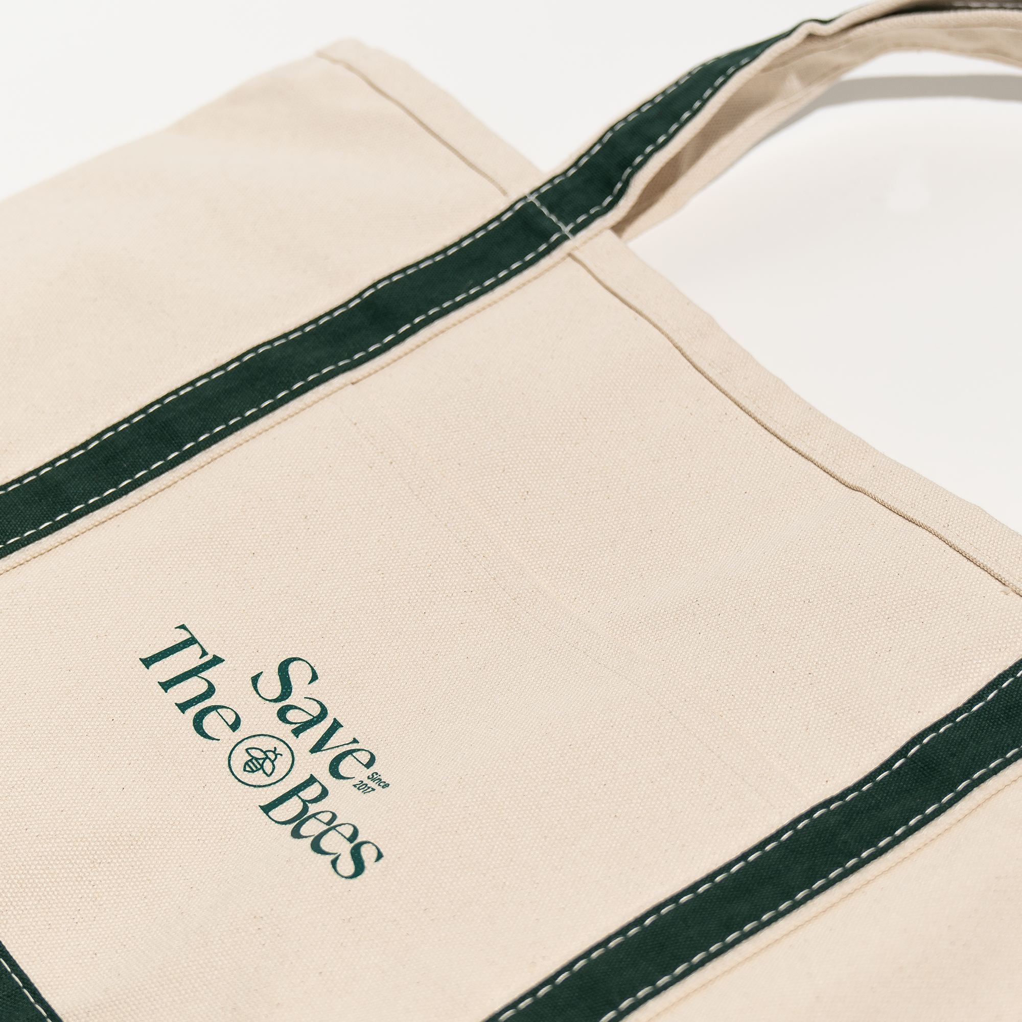 Close-up of the "Save The Bees" tote bag, showcasing the logo and dark green trim. Supports environmental causes.