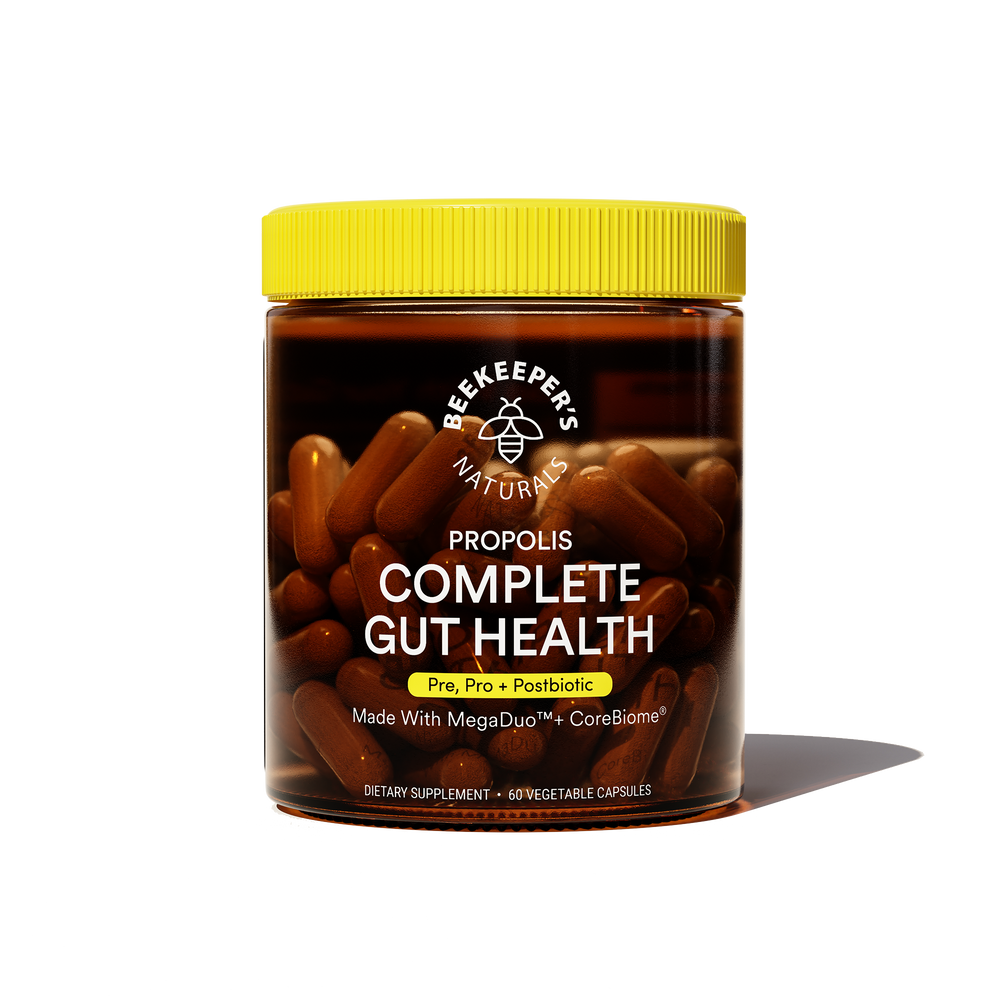 A jar of Beekeeper's Naturals Propolis Complete Gut Health supplements with capsules visible through the glass. The label is black and yellow with product information.