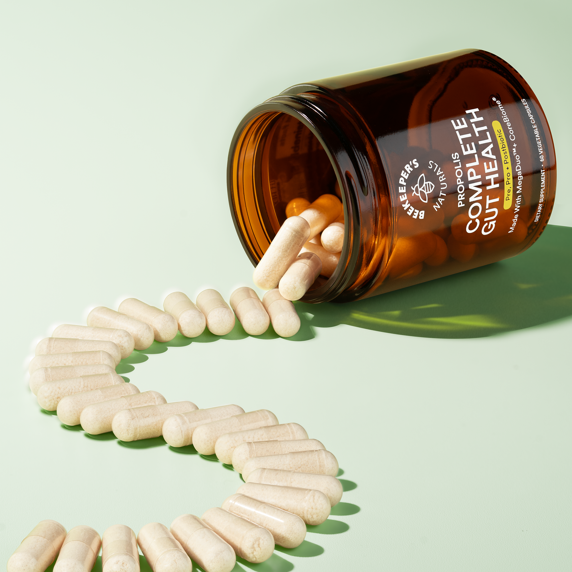 Beekeeper's Naturals Complete Gut Health capsules spilling from the bottle. Gut health supplement with pre-, pro-, and