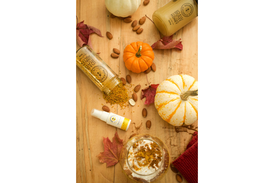 Fall flat lay of Beekeeper's Naturals bottles and spray with pumpkins, almonds, bee pollen and a spiced latte on a wooden table