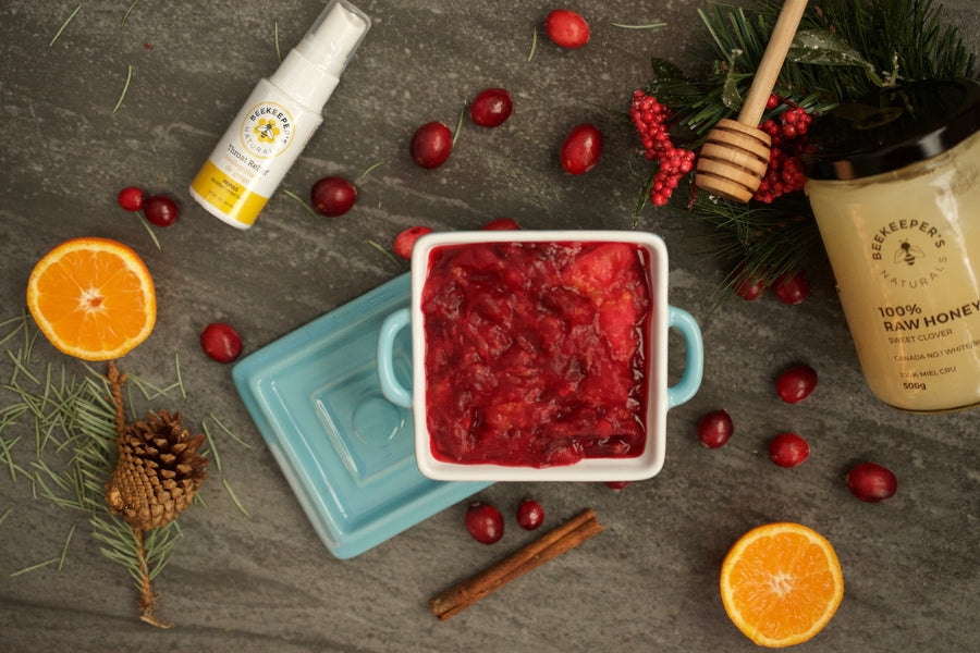 Cranberry sauce in a white dish with Beekeeper's honey jar, orange halves, cinnamon stick, fresh cranberries