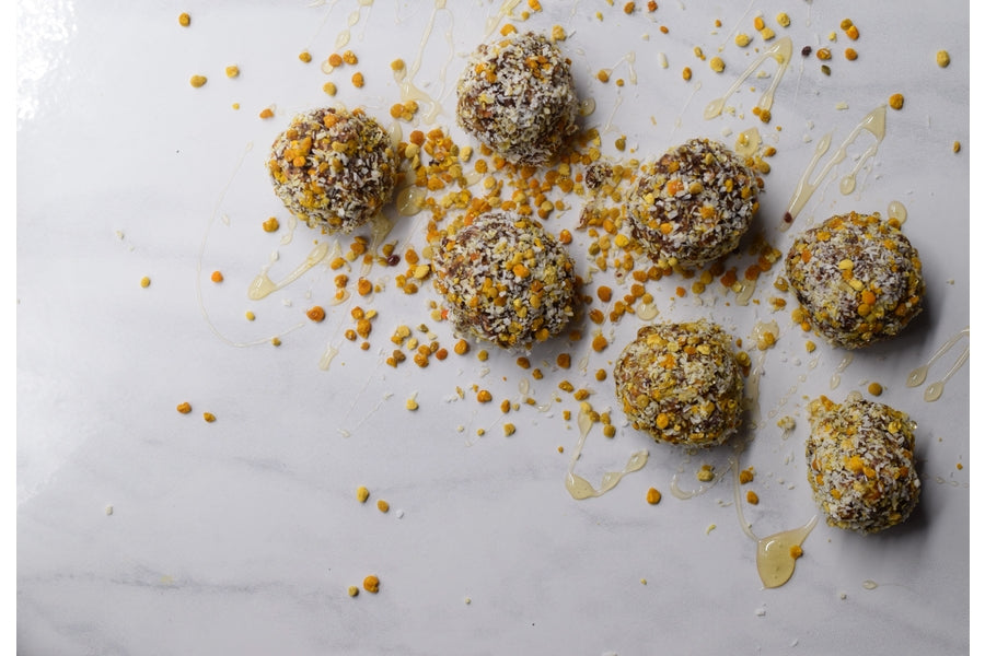 Overhead view of holiday snowball treats showcasing coconut flakes and bee pollen coating on a white marble surface