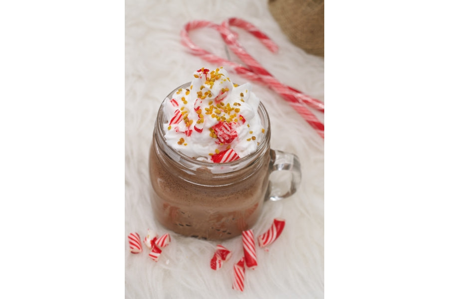 Peppermint hot chocolate in a mason jar topped with whipped cream, crushed candy cane and bee pollen on a white fur surface