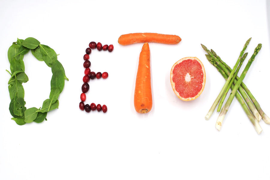 Banner spelling DETOX with greens, cranberries, carrots, halved grapefruit, and asparagus on white background