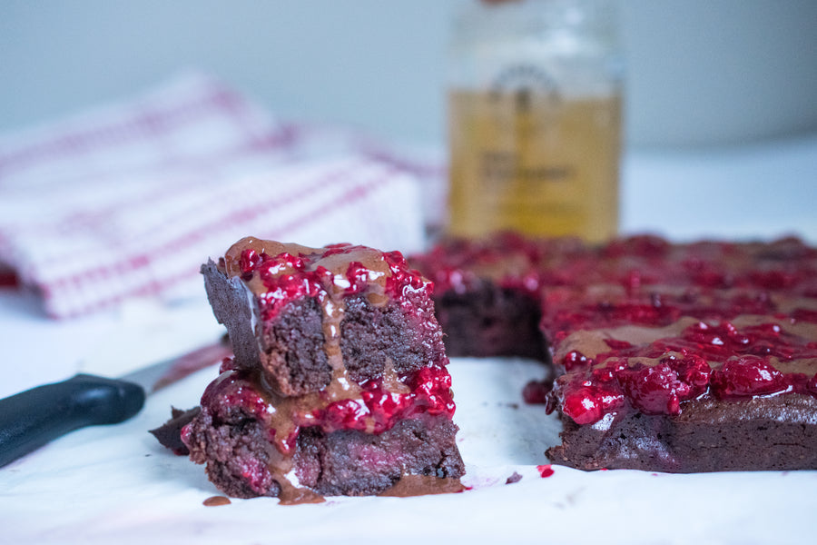 Close-up of stacked chocolate raspberry brownies showing gooey interior, raspberry compote and honey drizzle on parchment