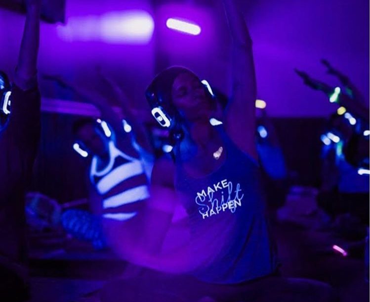 People wearing wireless headphones practicing yoga in a purple-lit silent disco style class