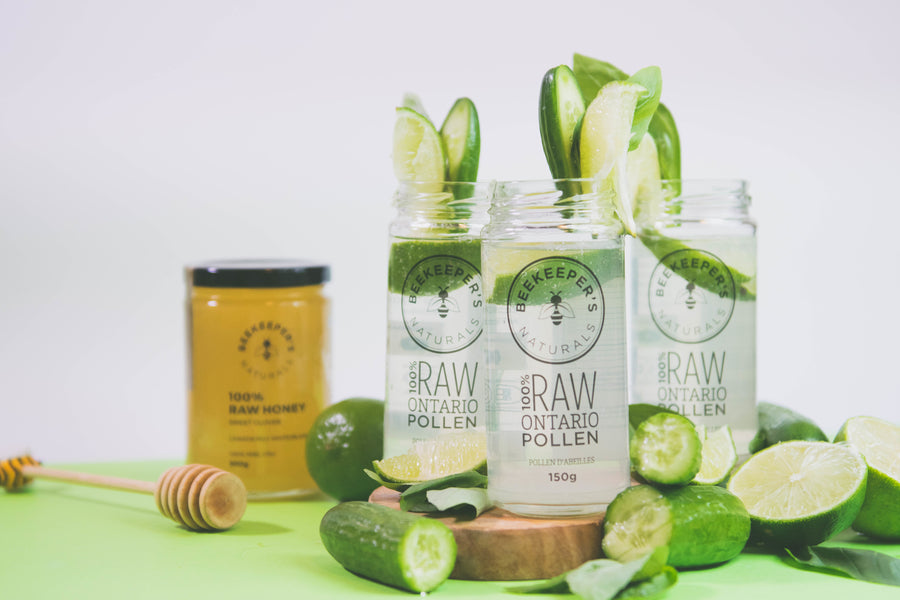 Three green cocktails in jars with raw Ontario pollen, garnished with lime and cucumber, honey jar behind