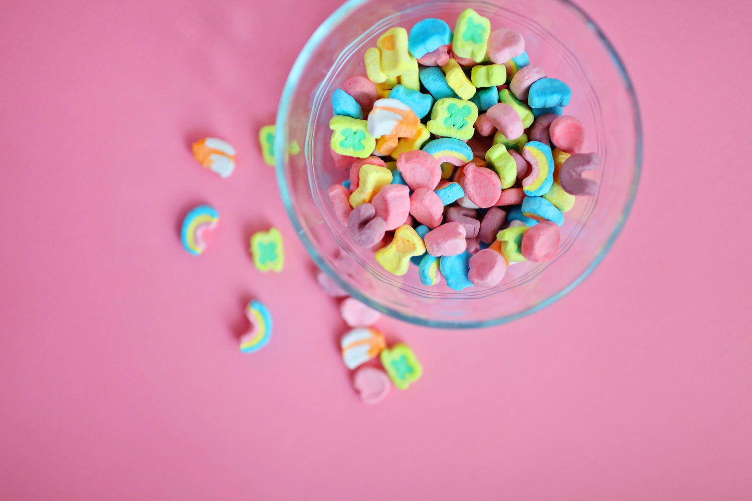 Glass bowl of pastel rainbow marshmallow candies spilled on a pink background, bright playful blog header