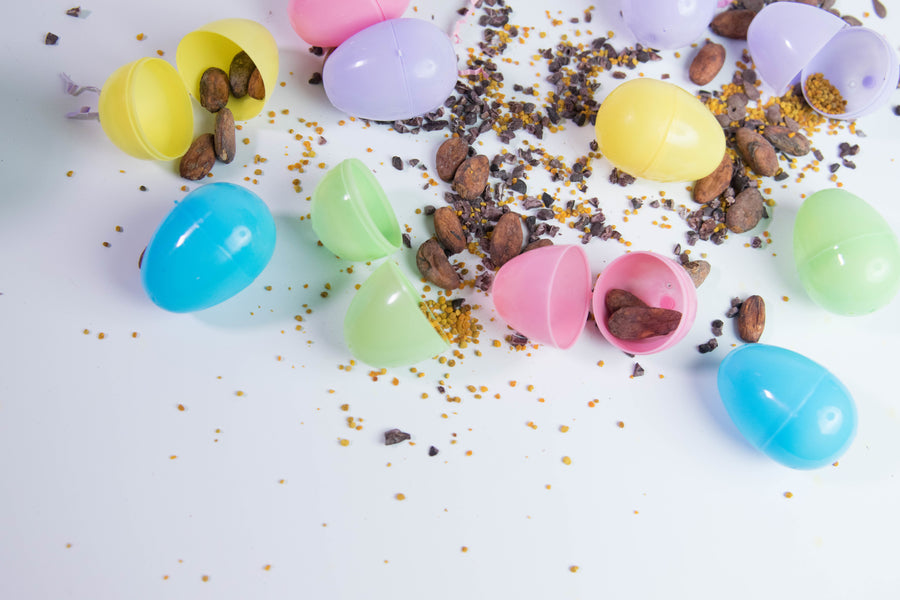 Pastel plastic Easter eggs spilled open with almonds, cacao nibs, and bee pollen on a white surface