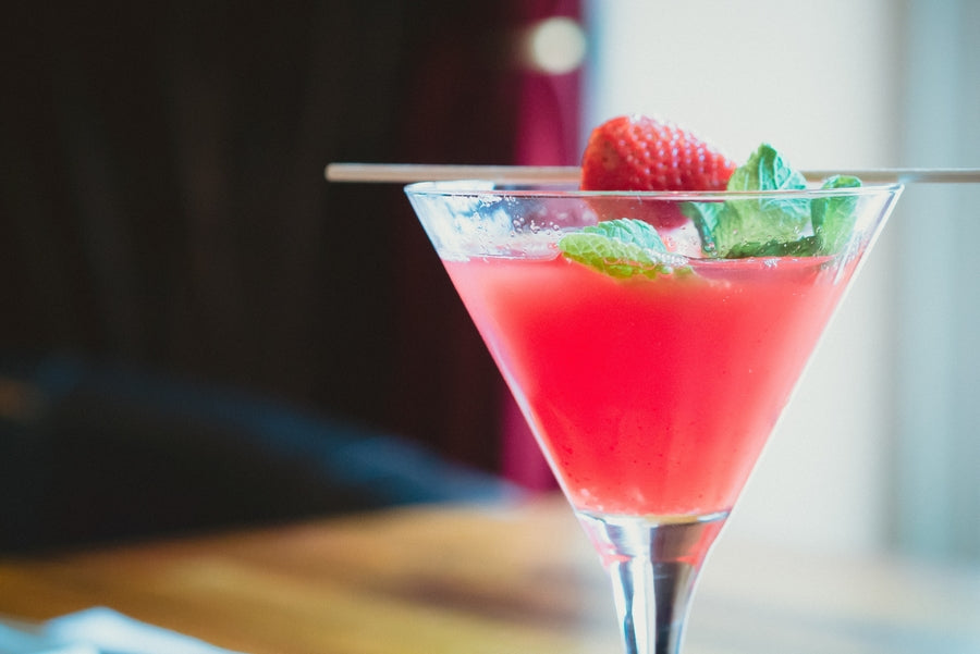 Close-up angled view of a pink margarita in a martini glass with strawberry and mint garnish, blurred background