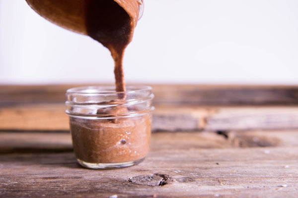 Hazelnut spread being poured into a small glass jar on a rustic wooden table