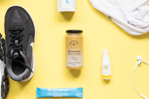 Flat lay of workout gear and Beekeeper's Naturals products including a jar of Bee Powered and a collagen peptide packet on a yellow background