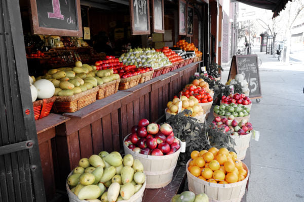 Outdoor market produce stand displaying baskets of apples, pears, oranges and other fruits along a sidewalk