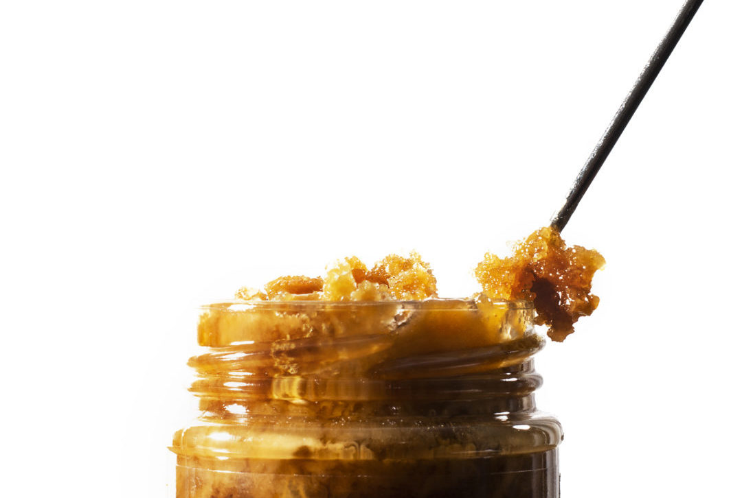 Close-up of open glass jar of crystallized honey with thick golden crystals on a spoon against a white background