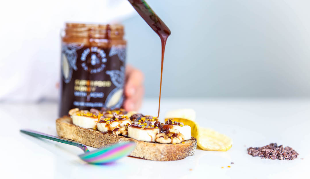 Banana and nut-butter toast with honey being drizzled from a spoon, jar blurred in the background on a white countertop