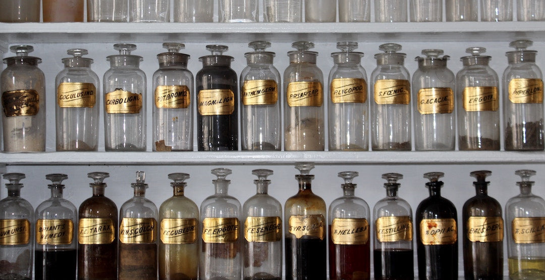 Rows of vintage apothecary bottles with gold labels on white shelves suggesting herbal remedies