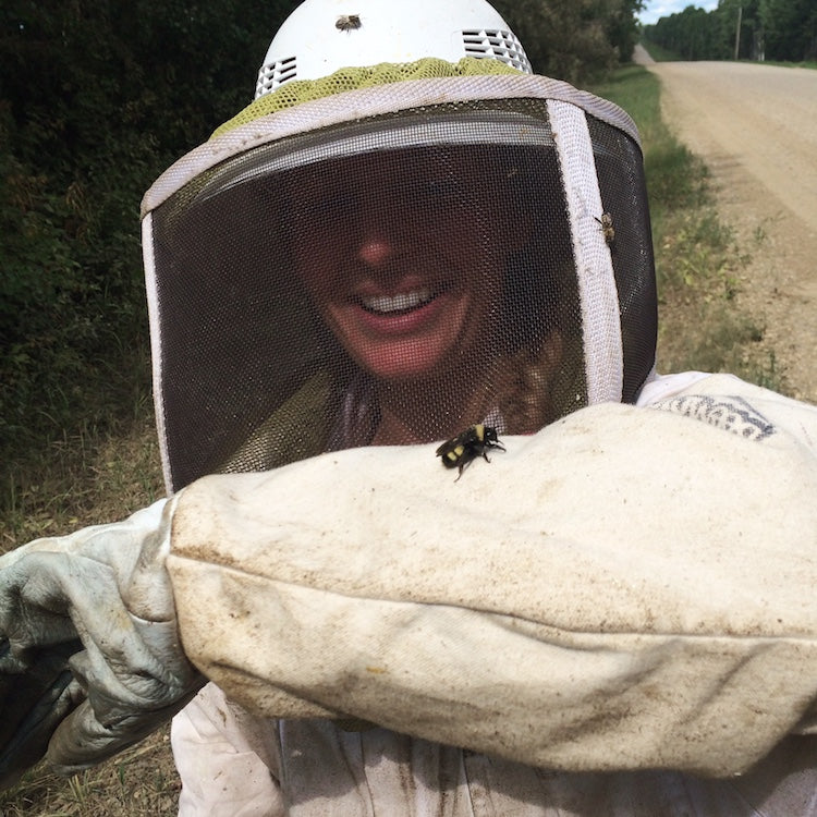 Stephanie Taylor smiling in beekeeper veil and heavy glove with a bumblebee on her glove on a country road