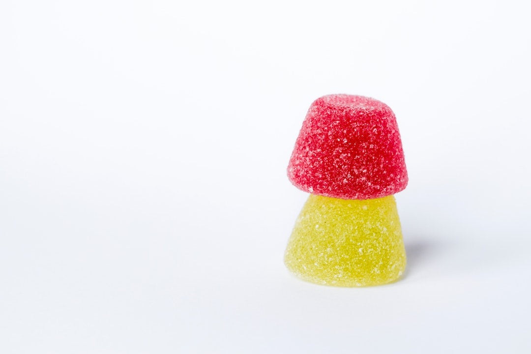 Front view of two sugar-coated gumdrop candies stacked with a red gumdrop on top of a yellow one on a white background