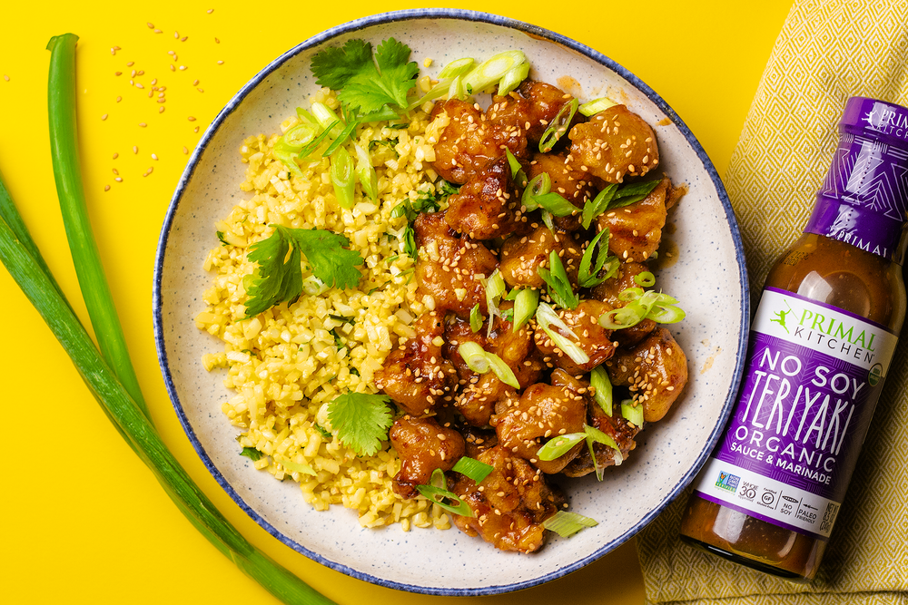General Tso’s cauliflower served with cauliflower rice, garnished with scallions and sesame seeds on a bright yellow background
