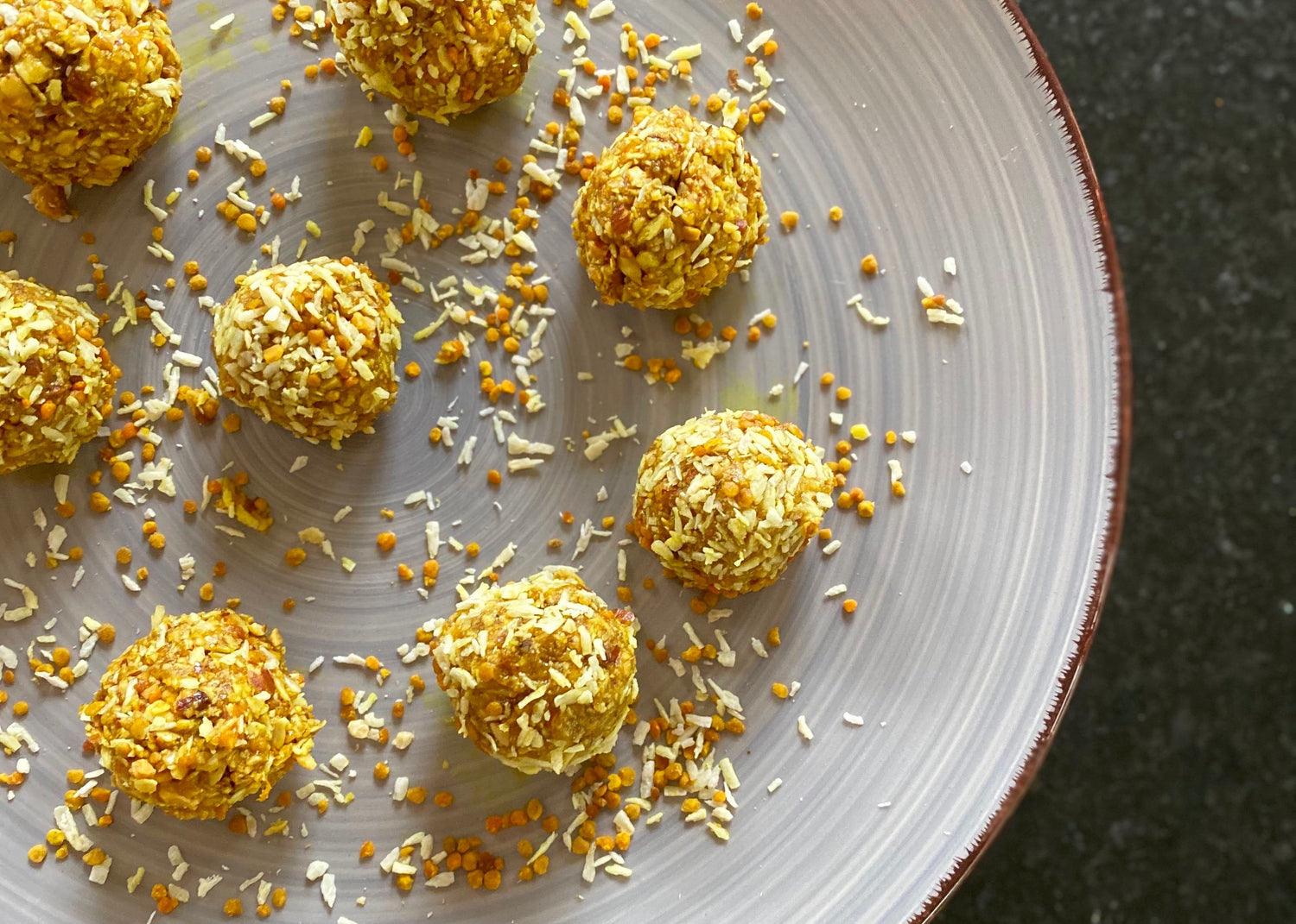 Top-down view of golden energy bites rolled in shredded coconut and bee pollen on a gray ceramic plate