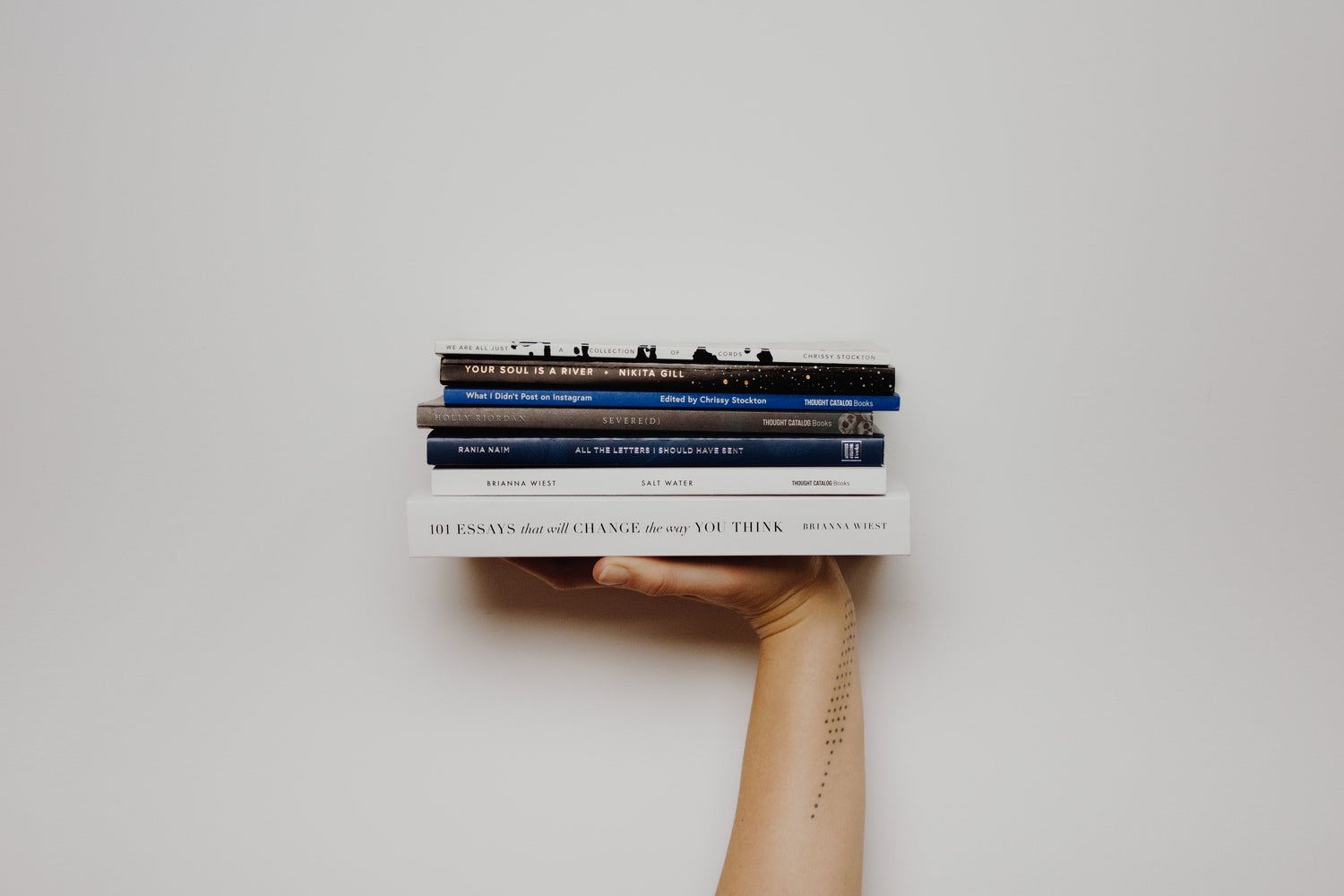 Hand holding a stack of five books including 101 Essays That Will Change the Way You Think against a white background