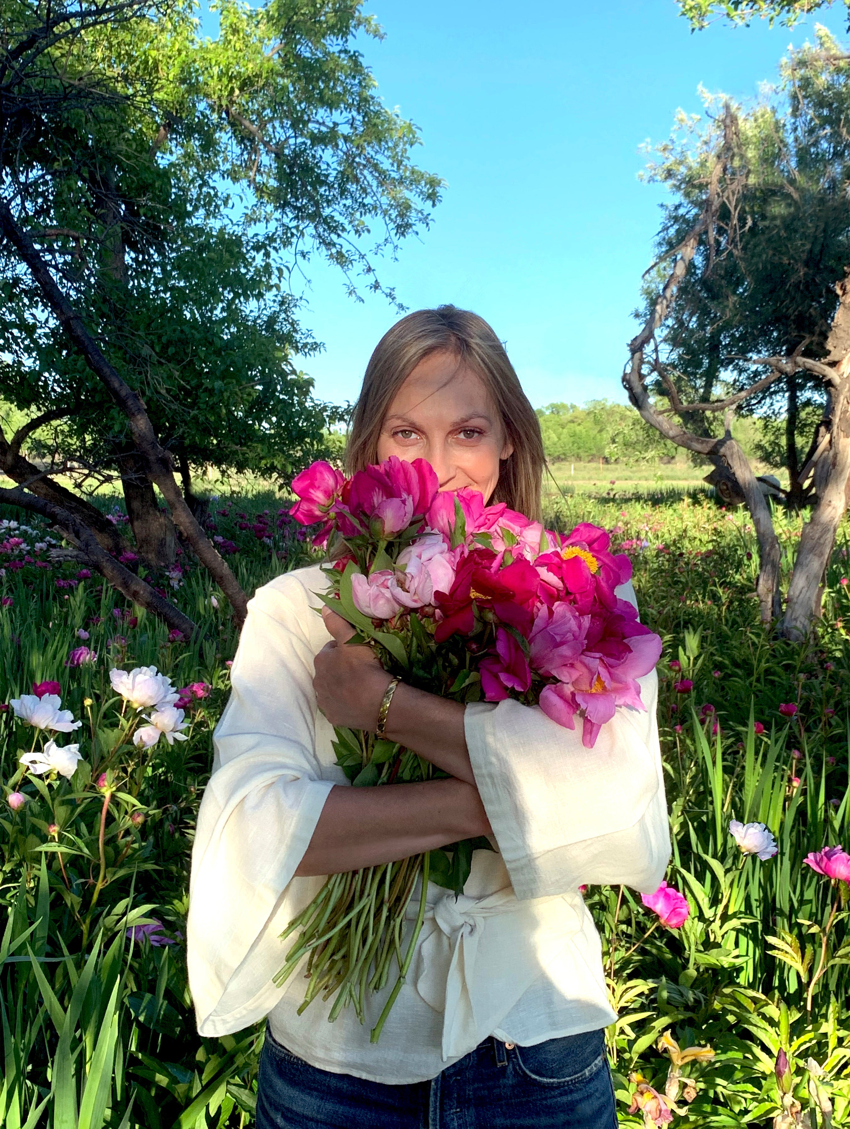 Woman holding a bouquet of bright pink peonies in a sunlit flower field