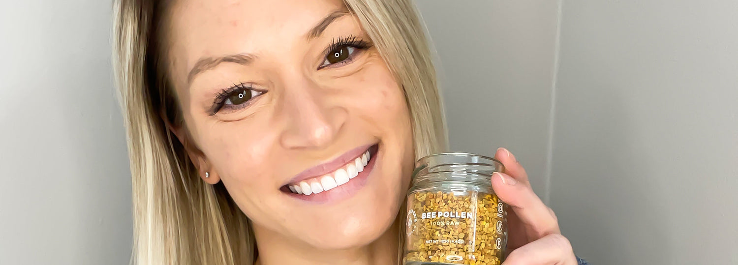 Woman smiling and holding a jar of bee pollen against a light gray background