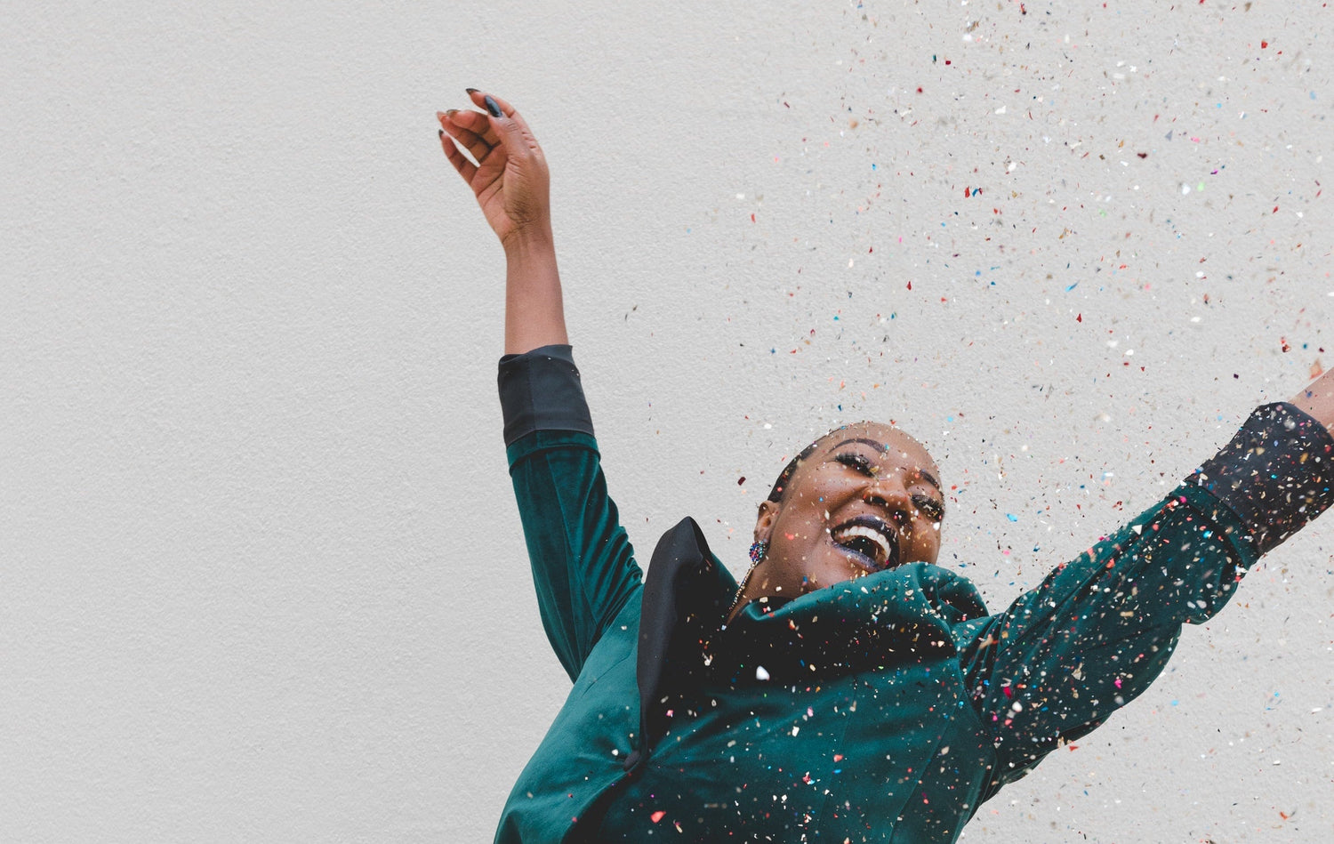 Woman joyfully throwing confetti and smiling against a light textured wall