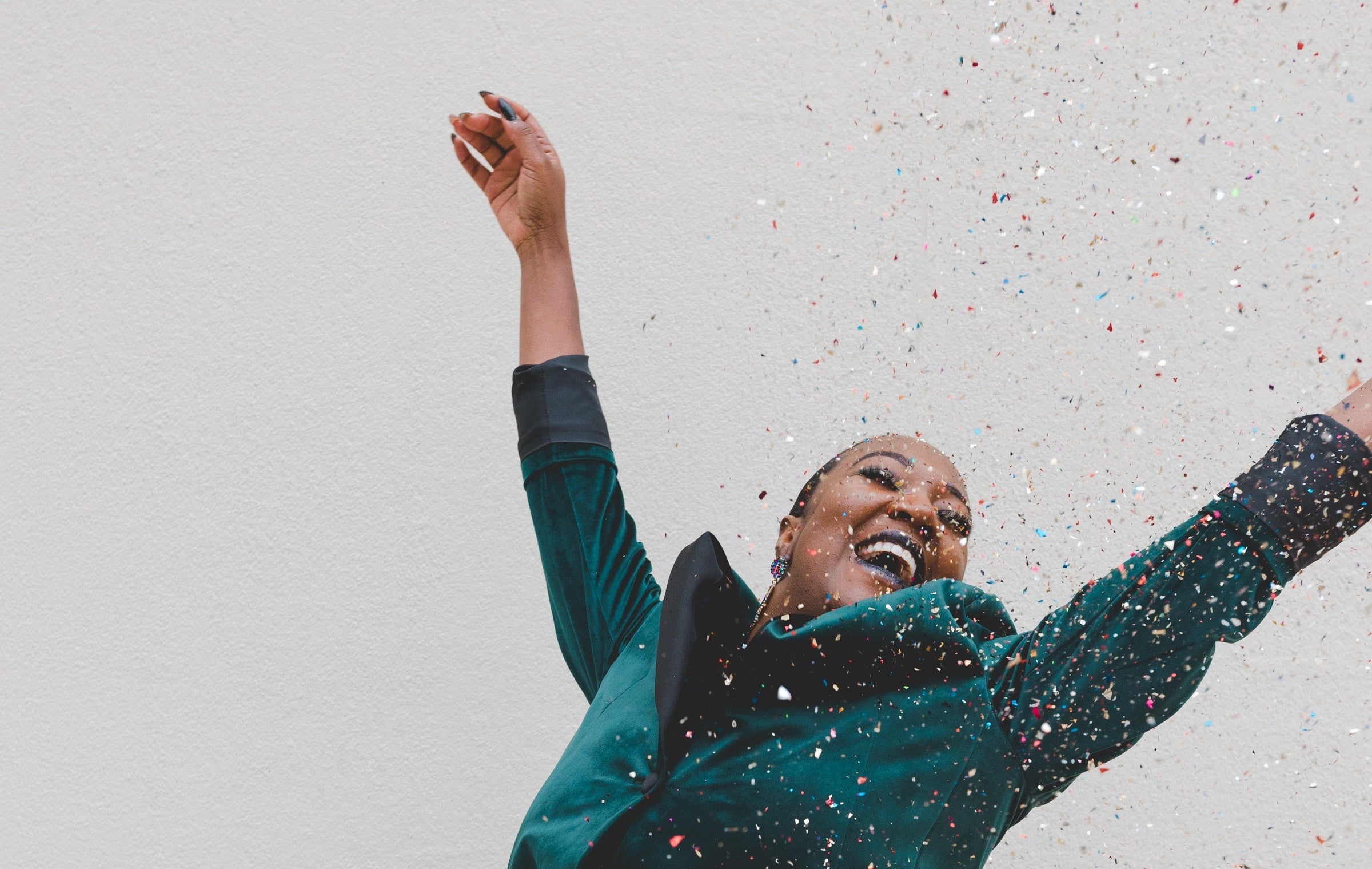 Woman joyfully throwing confetti and smiling against a light textured wall