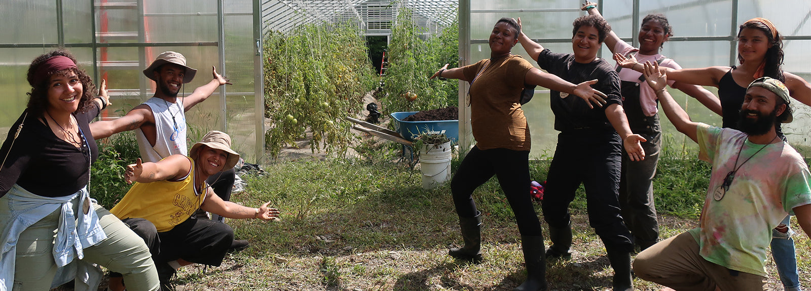 Group of community members posing with outstretched arms in front of a greenhouse at Soul Fire Farm
