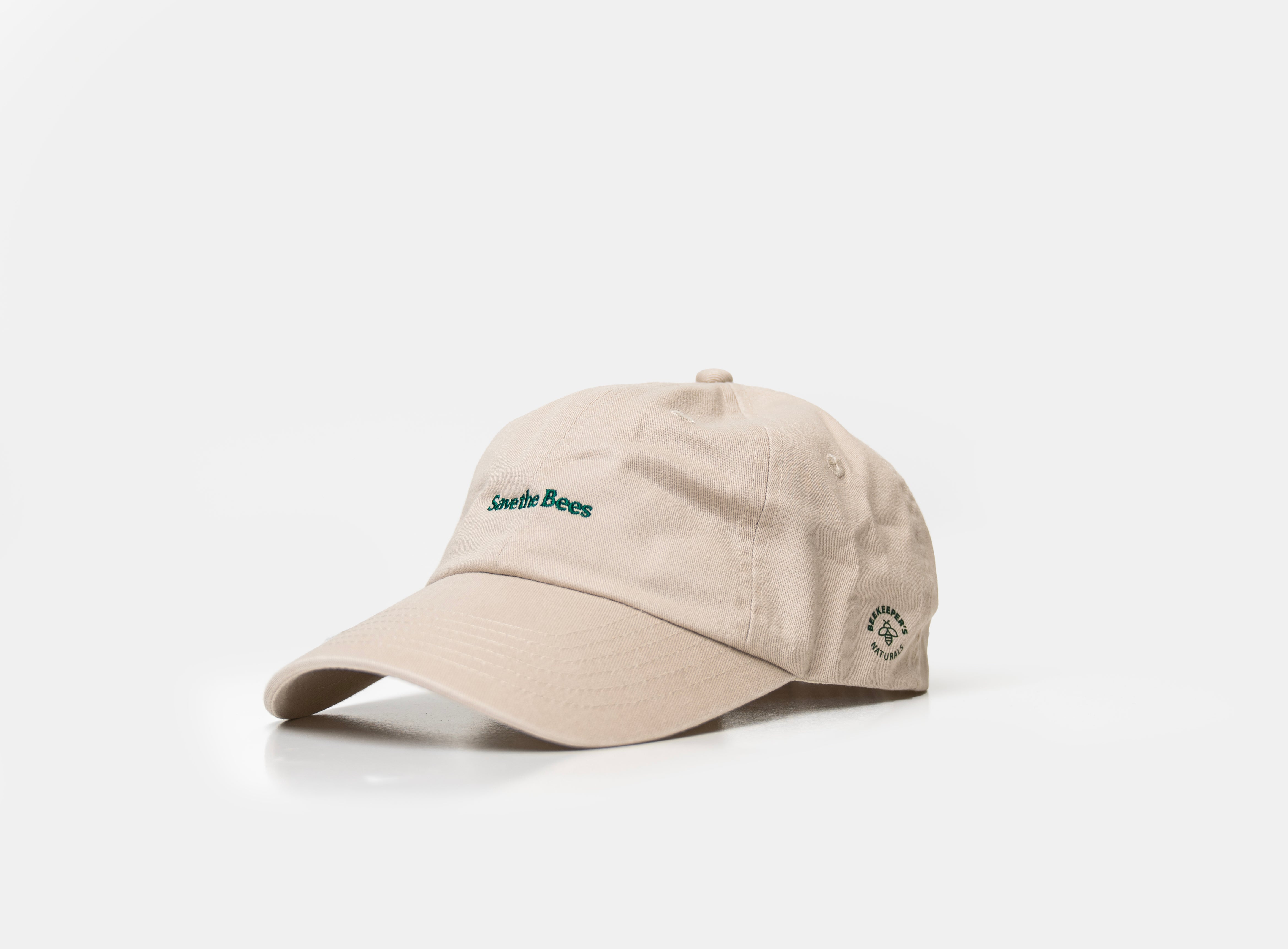 A light beige baseball cap with green embroidered 'Save The Boss' text on the front and a small circular logo on the side, photographed on a clean white background.