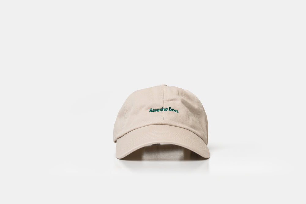 A beige baseball cap with 'Save the Bees' embroidered in green on the front, set against a plain white background.