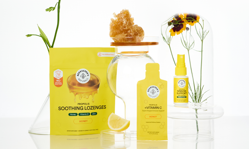 Honey and propolis wellness products arranged with flowers on a white background