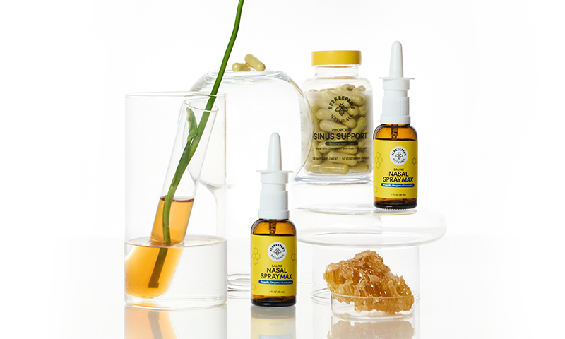 Sinus Support products and nasal spray bottles arranged with honeycomb and a flower on a white reflective background