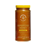 A jar of Beekeeper's Naturals Superfood Honey with a yellow lid, honeycomb patterns, and labels indicating propolis, bee pollen, and royal jelly as ingredients.