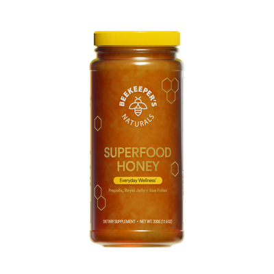 A jar of Beekeeper's Naturals Superfood Honey with a yellow lid, honeycomb patterns, and labels indicating propolis, bee pollen, and royal jelly as ingredients.