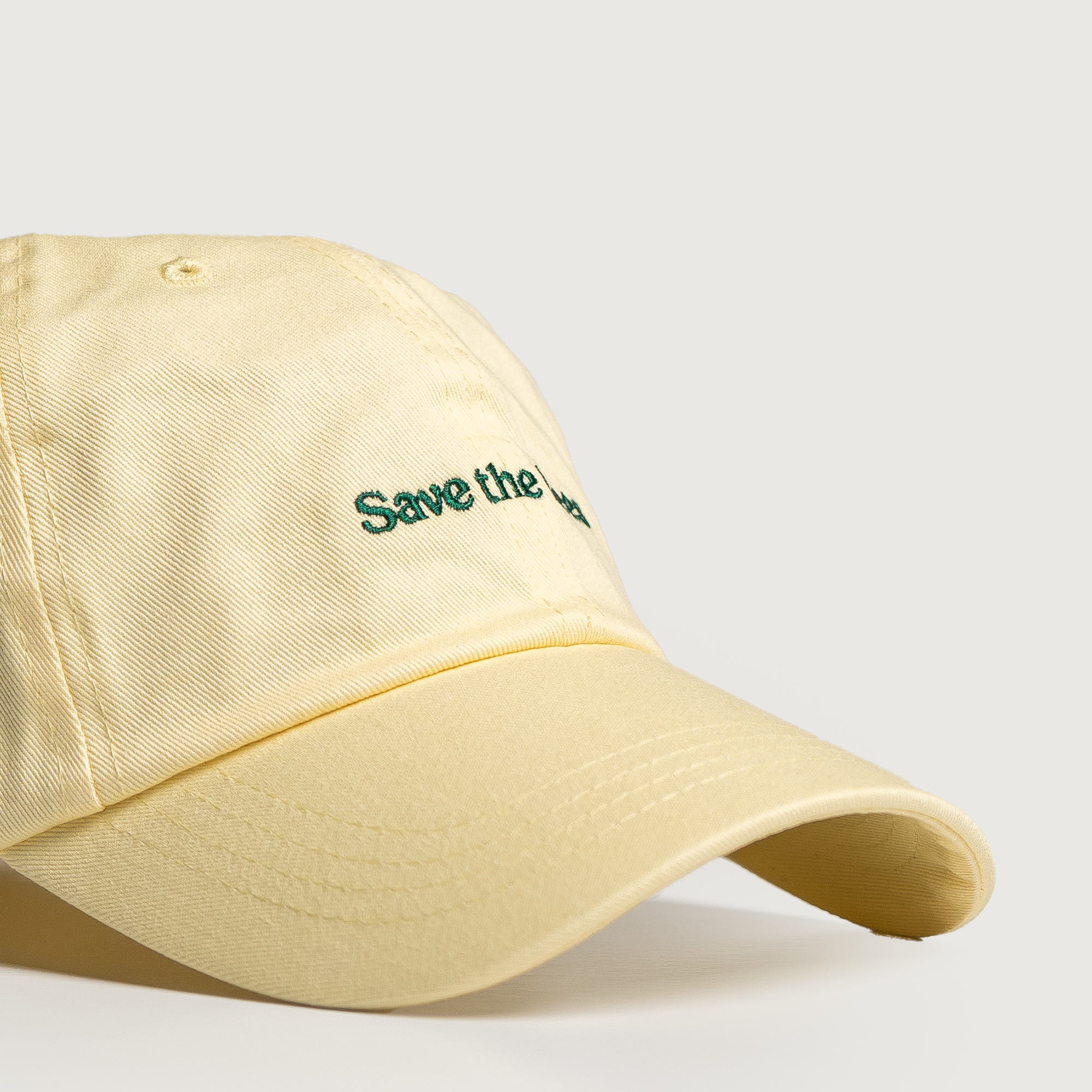 Three quarter view of Save the Bees hat in butter yellow with green embroidered text on light gray background