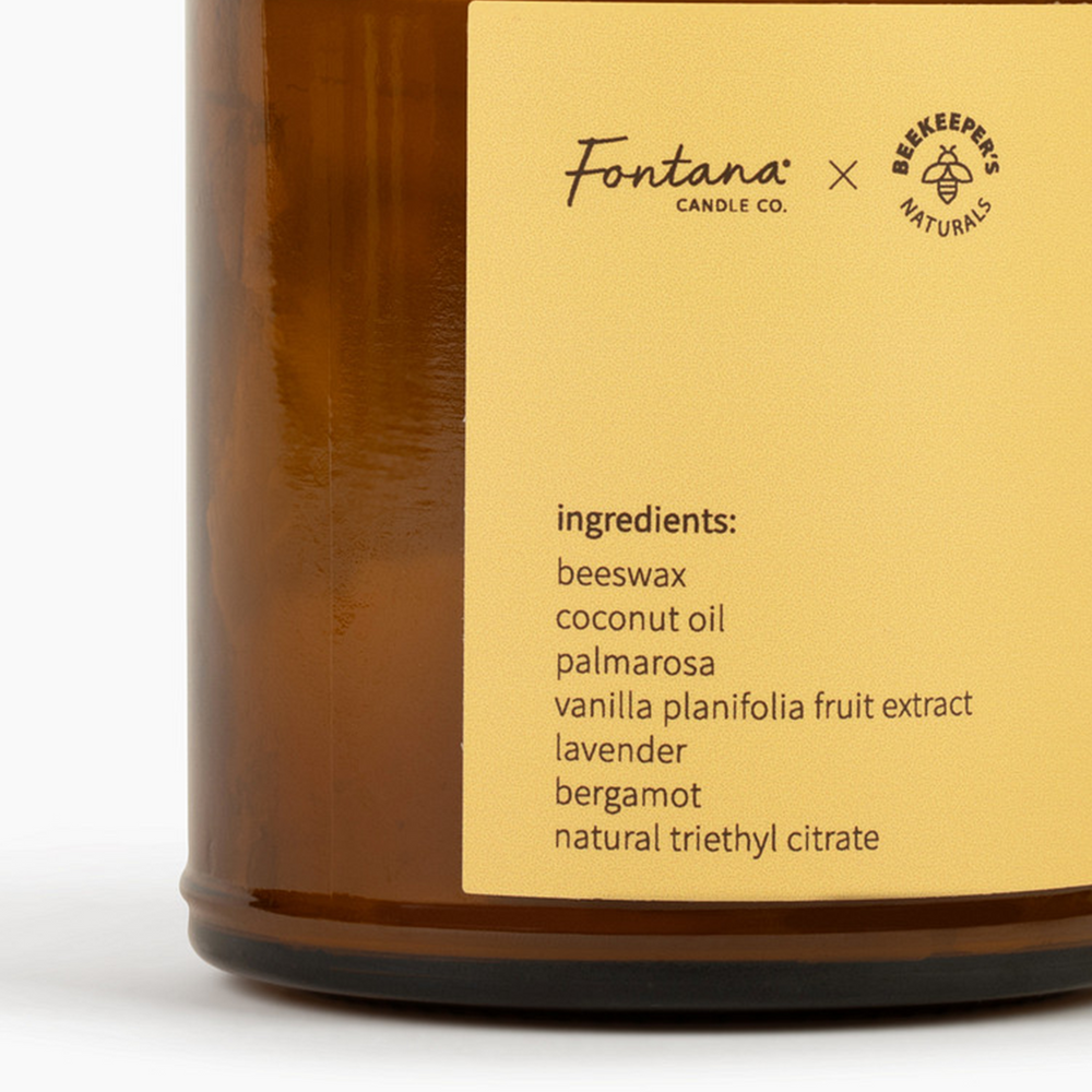 Close-up of Wildflower Honey Fontana candle showing label with logos and ingredients on white background