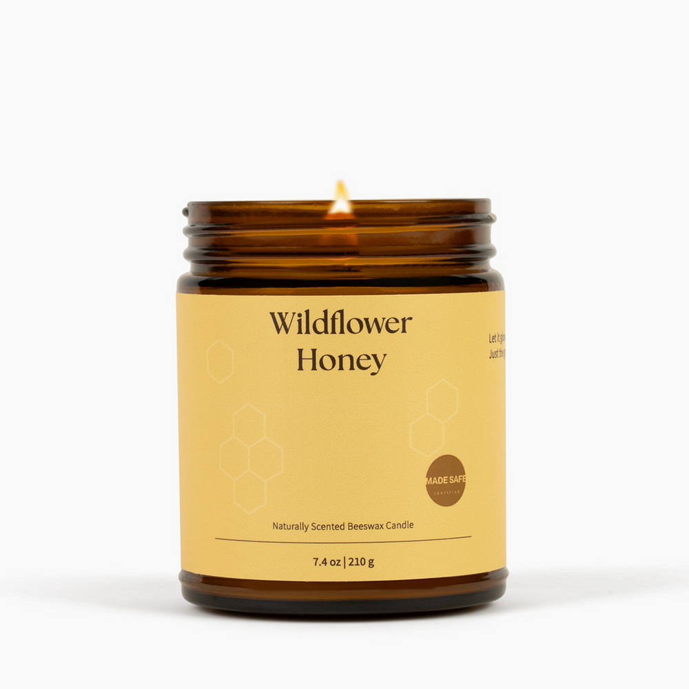 Candle in an amber jar labeled 'Wildflower Honey' on a white background