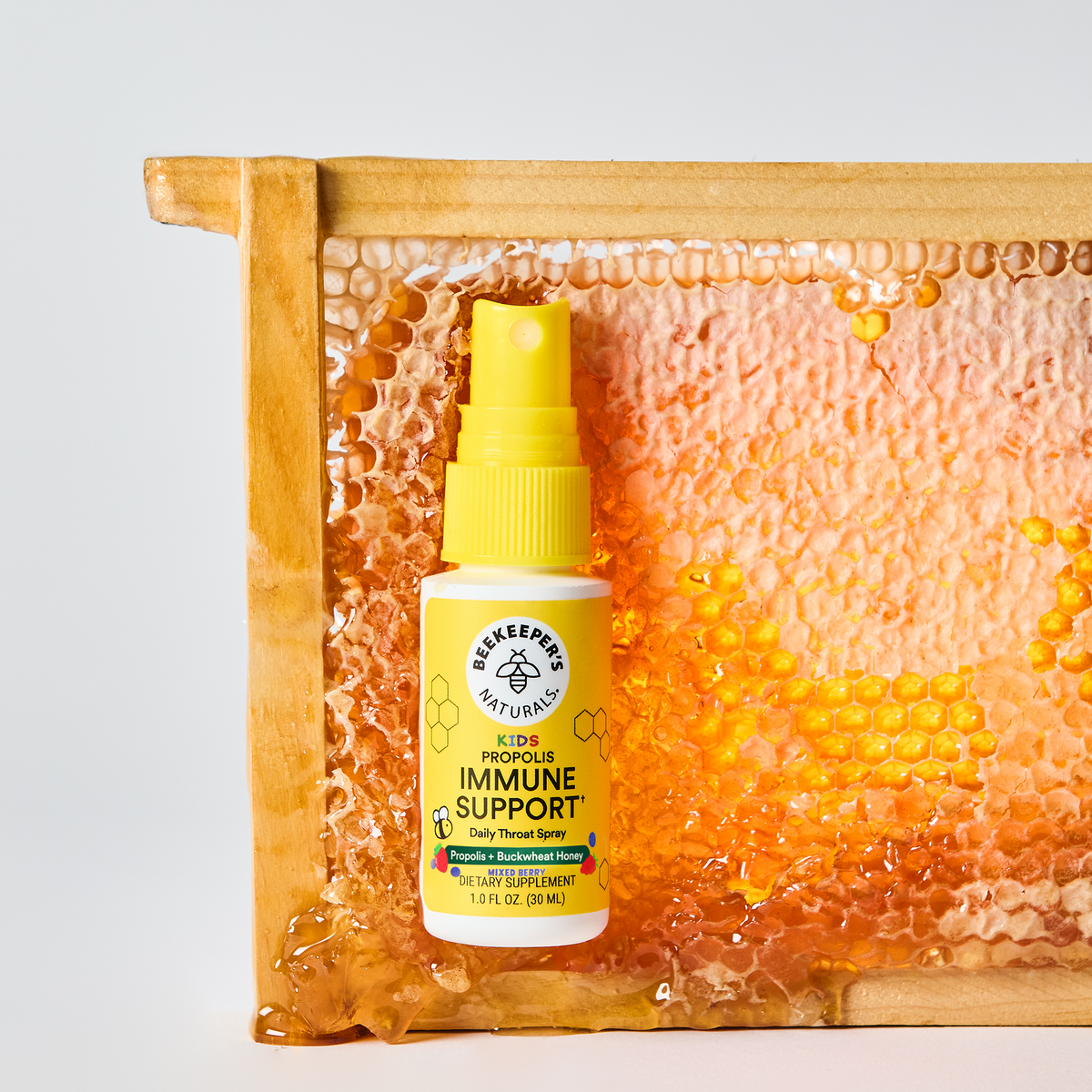 Front view of Kids Mixed Berry Propolis Throat Spray showcasing a yellow spray bottle with a honeycomb background