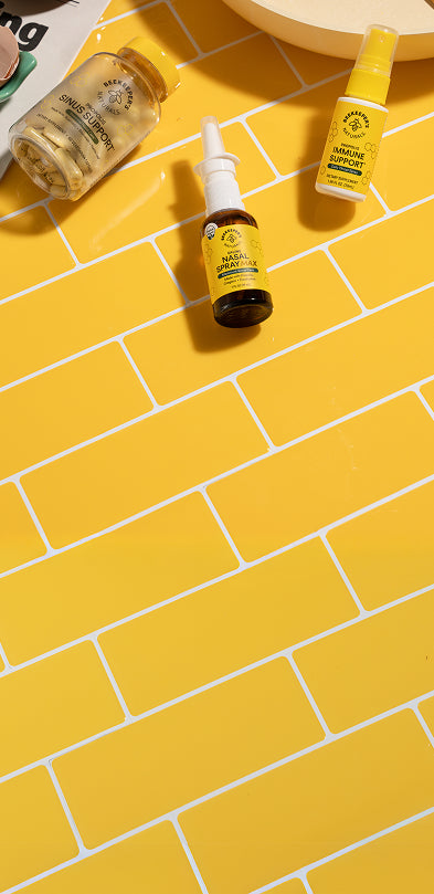 Three bottles of Beekeeper's Naturals products on a yellow tiled floor with eggs and a newspaper in the background.