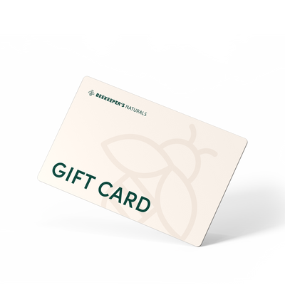 Angled view of Beekeeper's Naturals Hive gift card showing GIFT CARD text and botanical honeycomb pattern on cream background