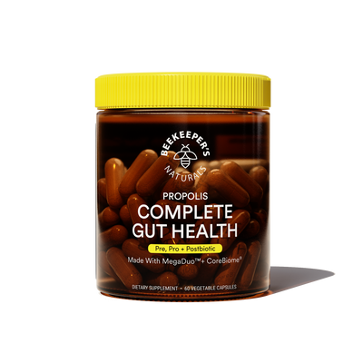 A jar of Beekeeper's Naturals Propolis Complete Gut Health supplements with capsules visible through the glass. The label is black and yellow with product information.